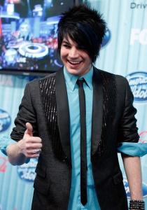 Adam Lambert wearing a blue shirt under a black suit jacket matched with a black neck tie